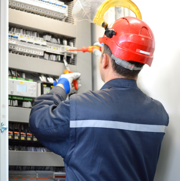 HOMME AVEC CASQUE ET GANT MANIPULANT DES OUTILS DANS UN TABLEAU ELECTRIQUE